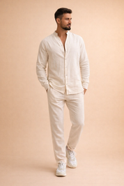 Off-white long-sleeve linen shirt with a relaxed band collar and front button placket, paired with matching off-white straight-leg linen trousers and clean white low-top sneakers