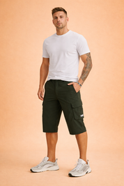 Men’s olive green knee-length cargo shorts crafted from smooth matte woven fabric with a solid, uniform color tone, featuring a tailored straight cut, belt-loop waistband with button closure, zippered side pocket, structured flap cargo pocket with stitched label detail, clean seam construction, and paired with white low-profile athletic sneakers for a modern outdoor-ready look.