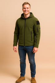 Olive green fleece zip-up jacket with multiple zippered pockets and hood, styled with slim blue jeans and tan suede boots.