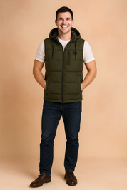 Men’s olive green sleeveless padded vest with hood, front zipper closure, and two side zip pockets, styled over a white t-shirt and dark denim jeans.