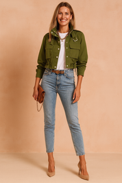 Olive green cropped utility jacket with silver button closures, drawstring waist ties, flap chest pockets, and structured collar, paired with a plain white crew-neck t-shirt and light blue high-waisted straight-leg jeans, styled with a tan leather belt featuring a leopard print accent.