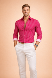 Fuchsia pink long-sleeve button-up shirt with fine vertical white pinstripes, open collar and rolled cuffs, paired with tailored white straight-leg trousers and a beige woven belt.