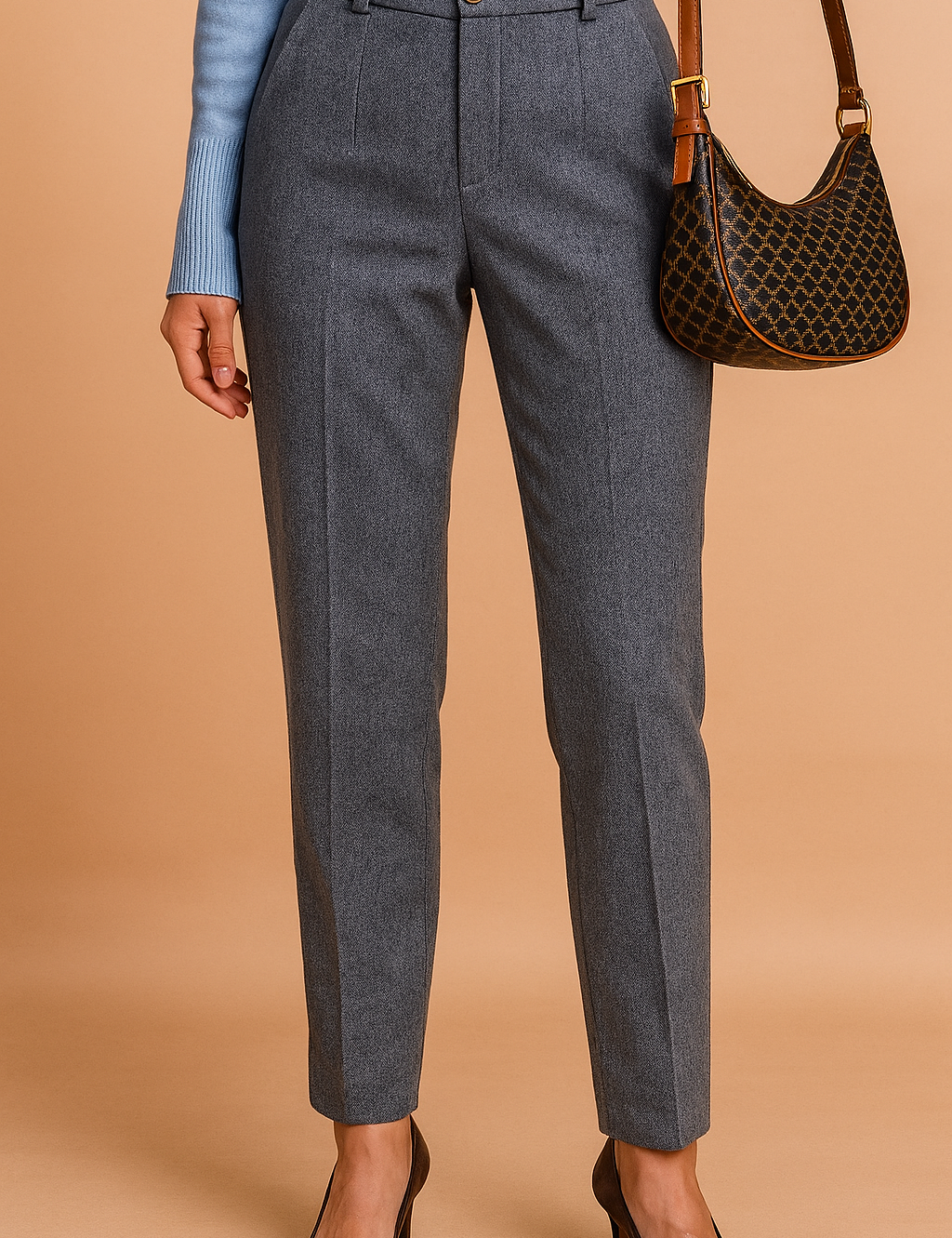 Tailored high-waisted grey herringbone trousers with a single front button, front pleats, belt loops, and tapered legs, styled with brown pointed-toe heels.