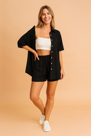 Relaxed black two-piece loungewear set featuring a short-sleeved button-up shirt with a front pocket and matching drawstring shorts, styled for everyday comfort and laid-back elegance.