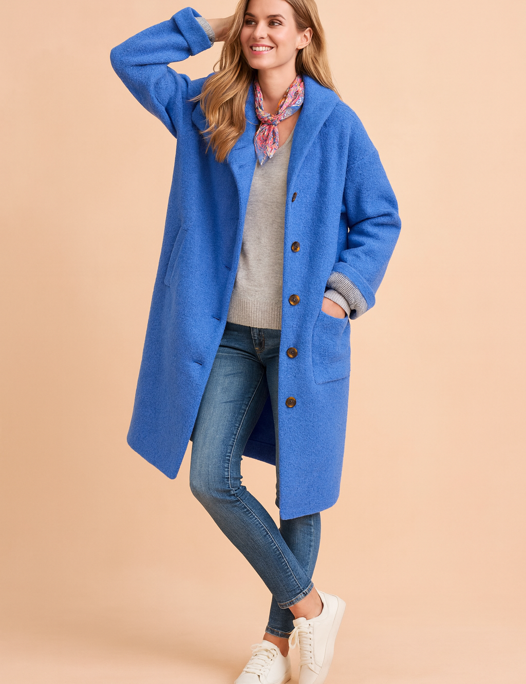 Bright blue button-up wool coat with rolled cuffs, side pockets, and long straight cut, styled over a light sweater and denim jeans.