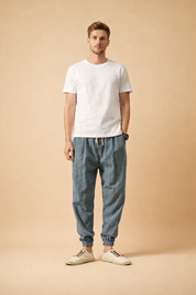Relaxed-fit men’s tapered trousers with elasticated cuffs, adjustable drawstring waistband, straight leg drape, clean front silhouette, lightweight woven texture, styled with low-profile casual lace-up shoes.