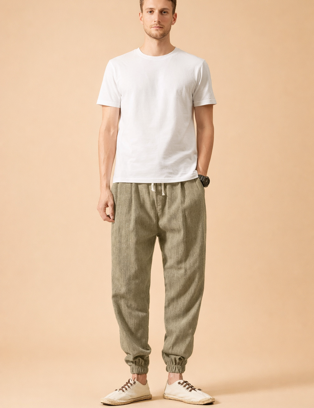 Men’s olive linen jogger trousers with elastic drawstring waist, relaxed tapered legs, ribbed ankle cuffs, paired with a plain white short-sleeve cotton T-shirt and low-profile beige lace-up casual shoes.