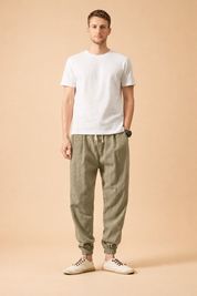 Men’s olive linen jogger trousers with elastic drawstring waist, relaxed tapered legs, ribbed ankle cuffs, paired with a plain white short-sleeve cotton T-shirt and low-profile beige lace-up casual shoes.