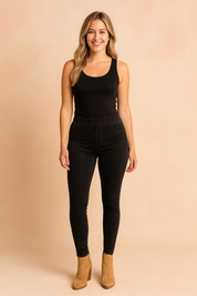Black high-waist jeggings with slim fit and faux front pockets, paired with a sleeveless black tank top and tan ankle boots for a sleek modern look.