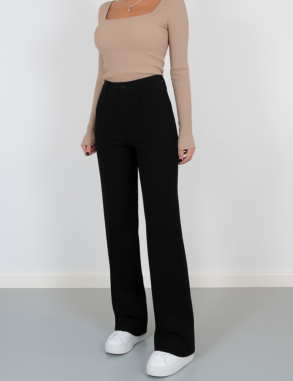 High-waisted black tailored trousers with front seam details and a wide-leg silhouette, paired with casual white sneakers for a polished minimalist look.