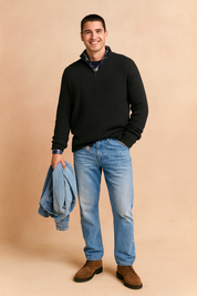 Men’s black ribbed knit half-zip pullover layered over a plaid shirt, styled with light blue jeans and brown suede boots, showcasing a classic casual winter outfit.
