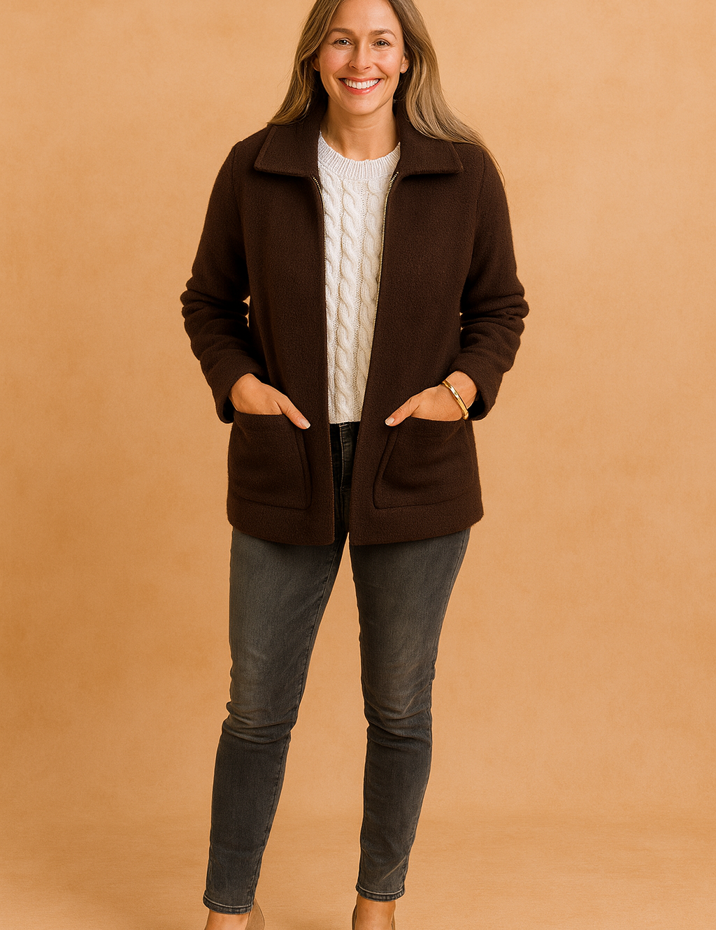 Dark brown zip-up jacket with wide collar and side pockets, layered over a white cable-knit sweater, styled with faded charcoal skinny jeans and taupe heels.