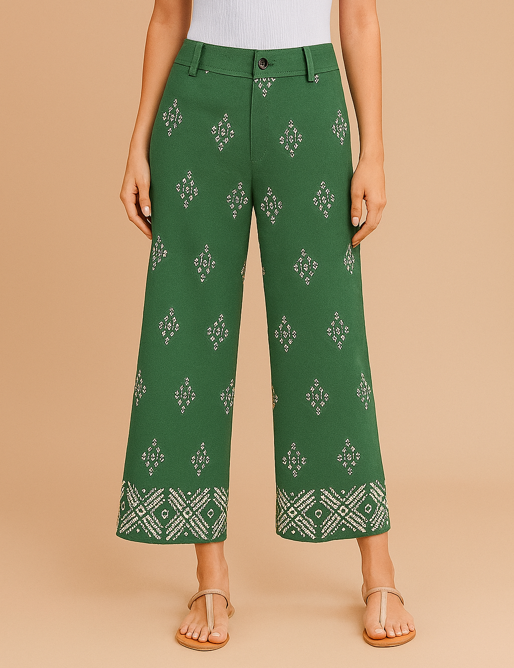 Green cropped wide-leg pants with symmetrical white geometric embroidery throughout and a detailed border pattern at the hem, featuring a high-rise waist with belt loops and front button closure, styled with beige sandals.