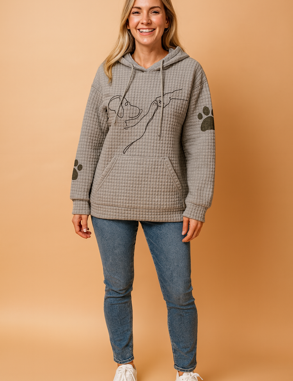 Grey waffle-knit hoodie featuring a minimalist dog and hand line art on the chest, paired with black paw print graphics on the sleeves; the top includes a front kangaroo pocket and drawstring hood, styled with light blue slim-fit jeans and white sneakers.