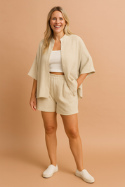 Beige textured linen two-piece lounge set featuring a loose short-sleeve button-up shirt with a high collar and matching high-waisted elastic shorts.