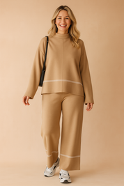 Two-piece khaki knit coord set featuring a boxy long-sleeve top with white piping detail and matching wide-leg trousers, styled with white sneakers and a black shoulder bag.