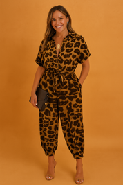 Leopard-print jumpsuit featuring a deep V-neckline, short sleeves, drawstring waist, and gathered ankle cuffs, accessorized with nude heels and a black clutch.