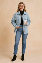 Light blue oversized button-up jacket with flap chest pockets, styled over a black turtleneck top, paired with fitted blue jeans and black ankle boots.
