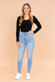 Women's outfit featuring a black long-sleeve fitted top paired with light blue high-waisted skinny jeans. The jeans have a classic five-pocket design and a slightly faded wash for a modern look, complemented by white low-top sneakers for a casual, stylish finish