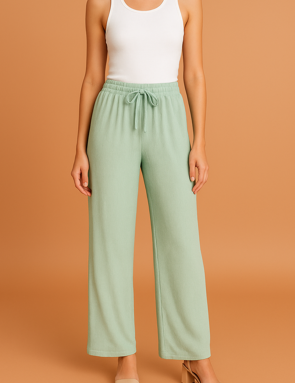 Light sage green wide-leg pleated pants with a ribbed texture and drawstring waistband, styled with a white tank top and nude block-heeled sandals.