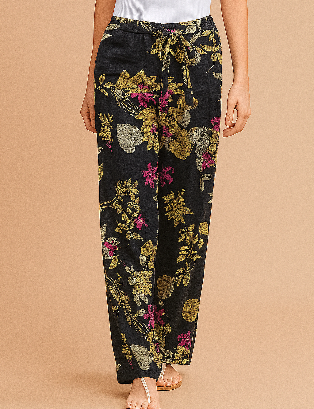 Wide-leg navy blue pants with a bold botanical floral print in green, pink, and beige, featuring a drawstring waist and relaxed fit, styled with beige thong sandals.