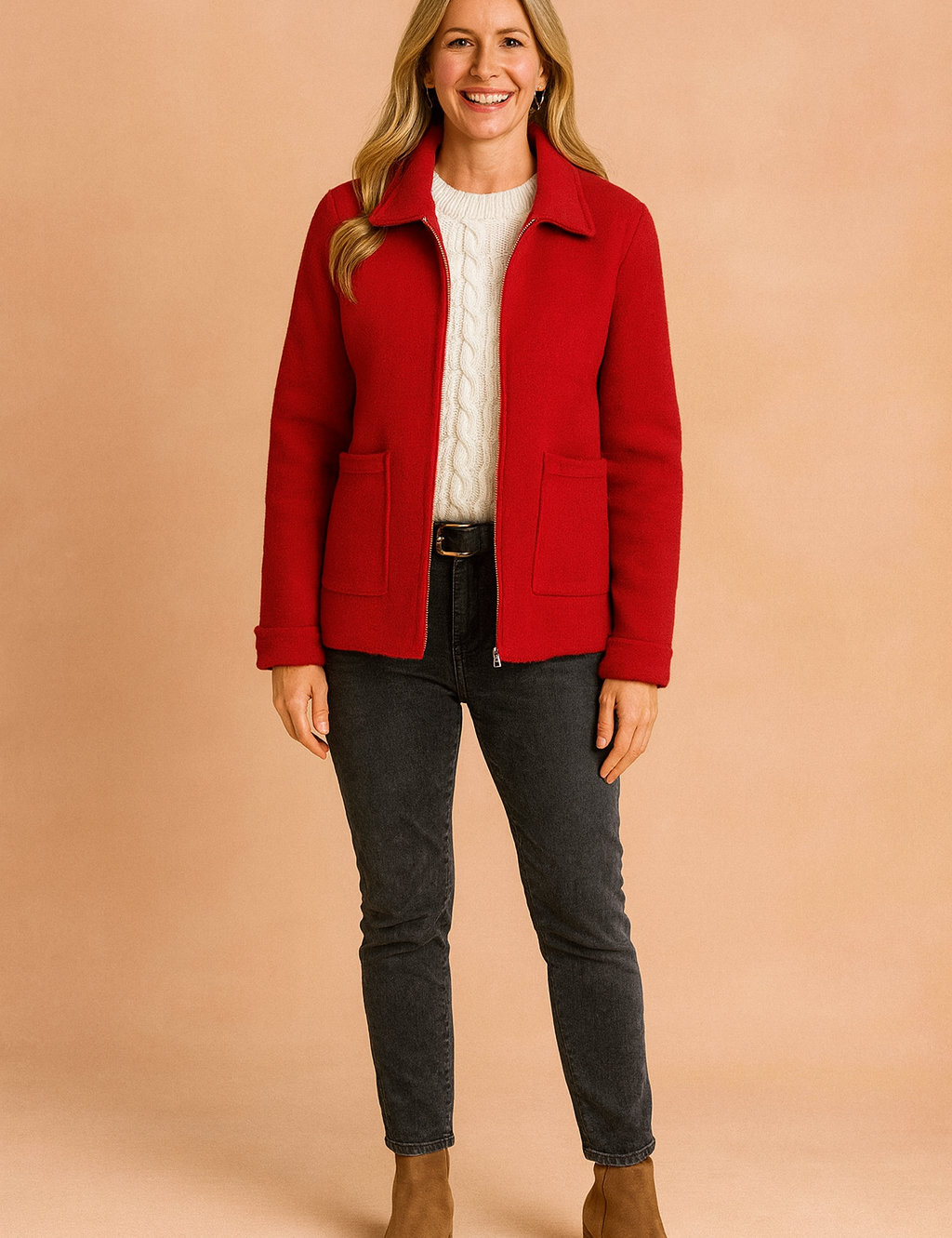 Red wool zip-up jacket with patch pockets layered over a cream cable-knit sweater, styled with washed black jeans and tan ankle boots.