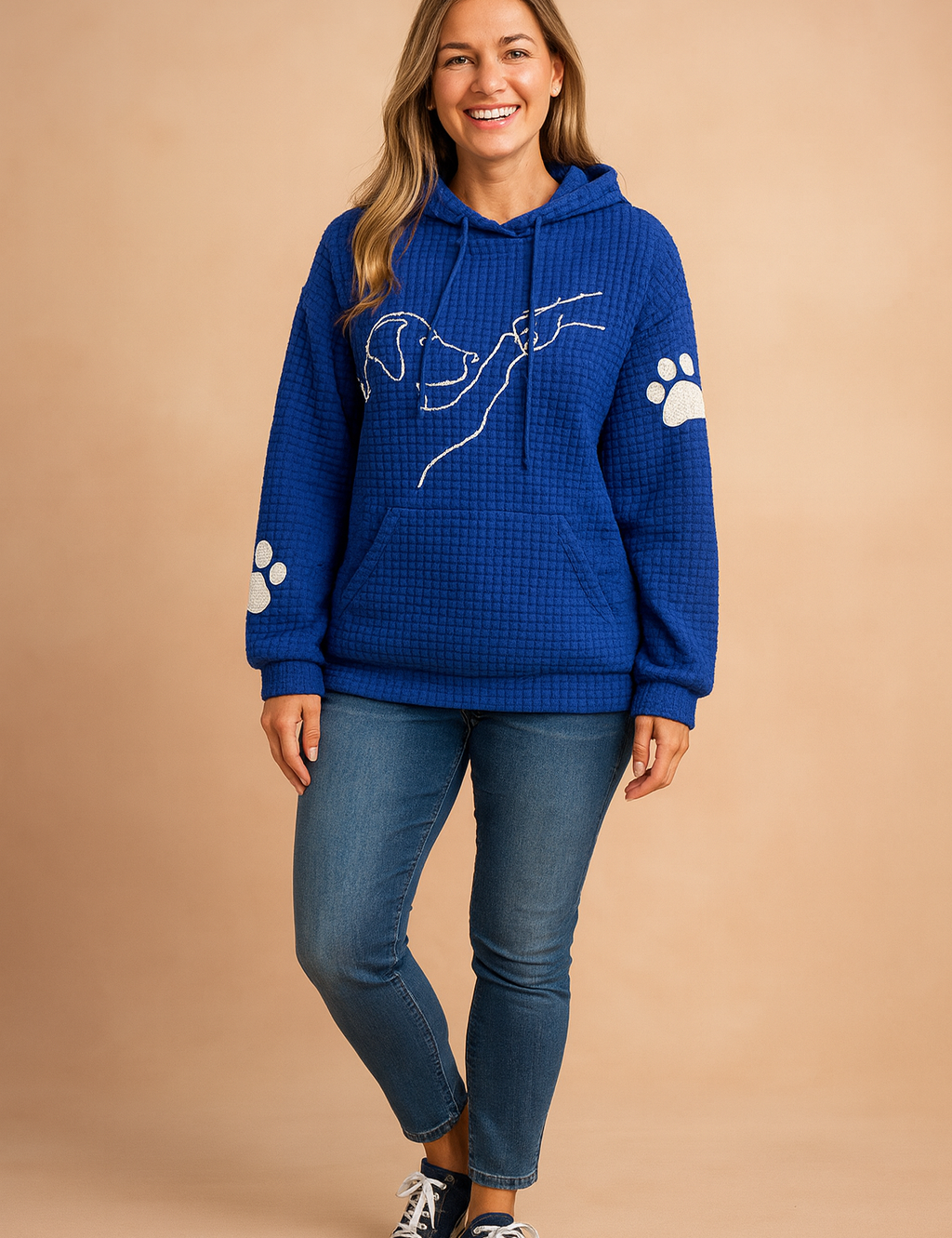 Royal blue waffle-knit hoodie with front kangaroo pocket, white minimal dog line art and paw print details on sleeves, styled with medium-wash skinny jeans and navy canvas sneakers.