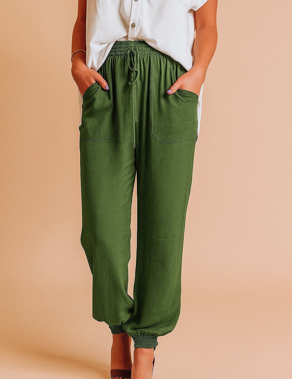 Olive green drawstring jogger pants with front patch pockets and elastic cuffs, styled with a tucked-in white button-up blouse and brown heeled sandals.