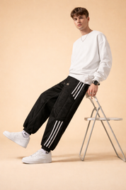 Relaxed-fit black jogger pants with elastic cuffs, clean straight silhouette, contrast side stripe detailing, and a smooth structured drape styled with low-top white sneakers.