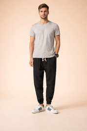 Relaxed-fit black tapered jogger pants with elastic cuffs and adjustable drawstring waist, styled with a minimalist short-sleeve top and clean low-profile sneakers for a modern everyday look.