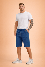 Solid deep blue knee-length casual shorts made from smooth lightweight fabric with an elastic waistband and white adjustable drawstring, featuring a clean matte finish with no pattern or print, paired with a solid olive green short-sleeve crew and white low-top athletic sneakers with breathable mesh panels and cushioned rubber soles.