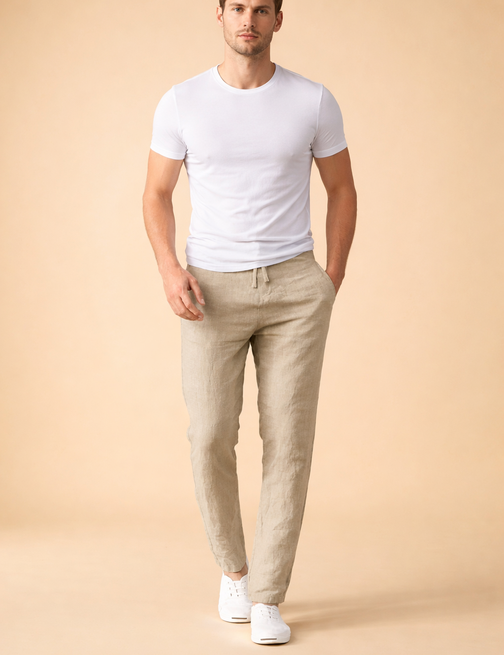 Light beige drawstring trousers with a relaxed straight-leg fit, smooth woven texture, clean waistband tie detail, and a minimalist silhouette styled with a plain white short-sleeve top and white low-profile sneakers.