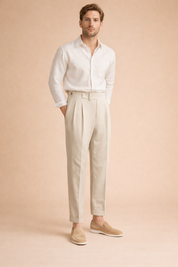 Light-toned pleated trousers featuring a high-rise waistband, front button closure, subtle texture, tailored leg shape, and cuffed ankle length styled with a lightweight long-sleeve shirt and clean loafers.