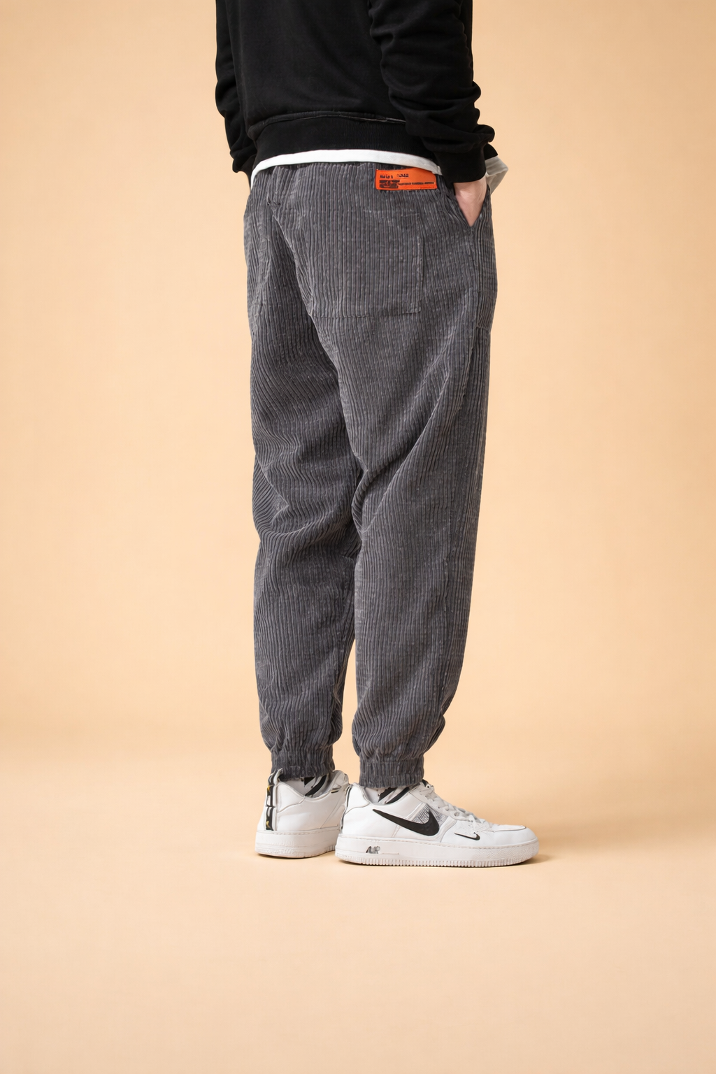 Relaxed-fit ribbed corduroy trousers with an elasticated waistband, straight leg cut, and gathered cuffs, styled with clean low-top sneakers for a modern casual look.