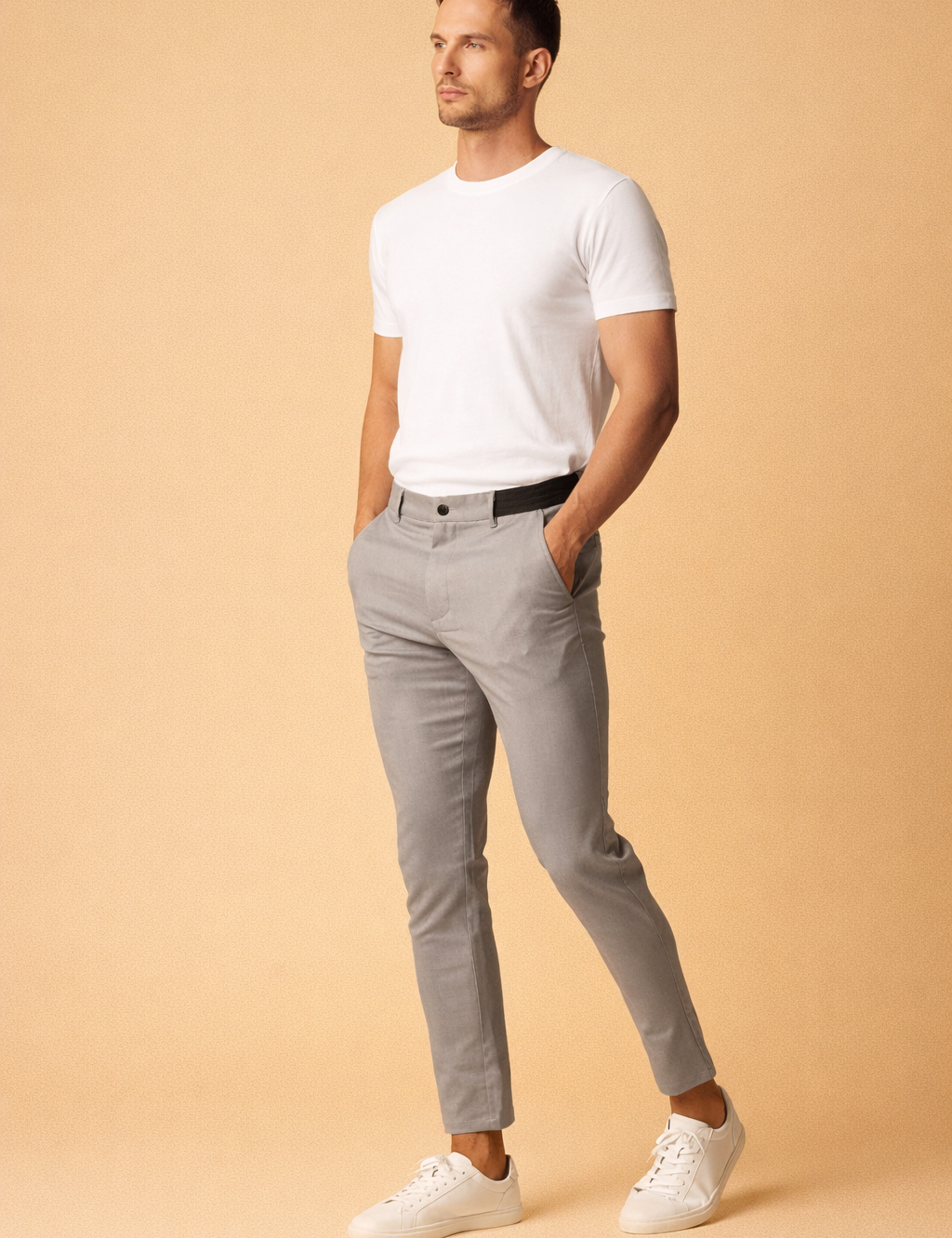 Slim-fit tailored grey trousers with a clean front closure, tapered leg, ankle-length cut, and minimalist silhouette paired with a plain white fitted top and low-profile white sneakers.