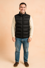 Black puffer vest for men styled with a high collar and front zipper pockets, layered over an off-white sweater for a warm, casual winter look.