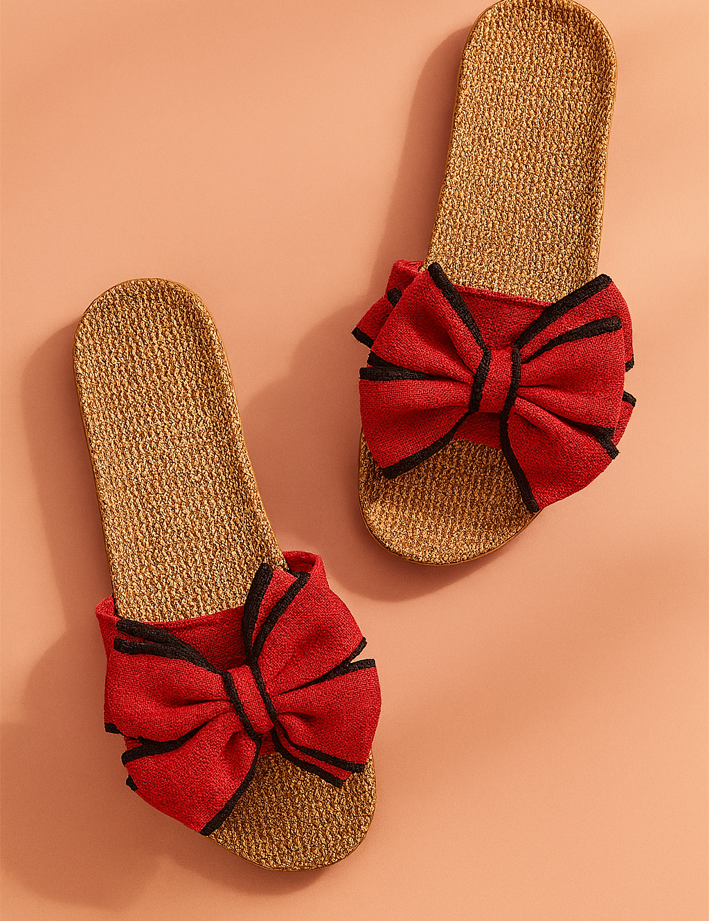Red bow slide sandals with woven jute soles and black-trim accents on the bows, designed for a casual yet bold summer look.