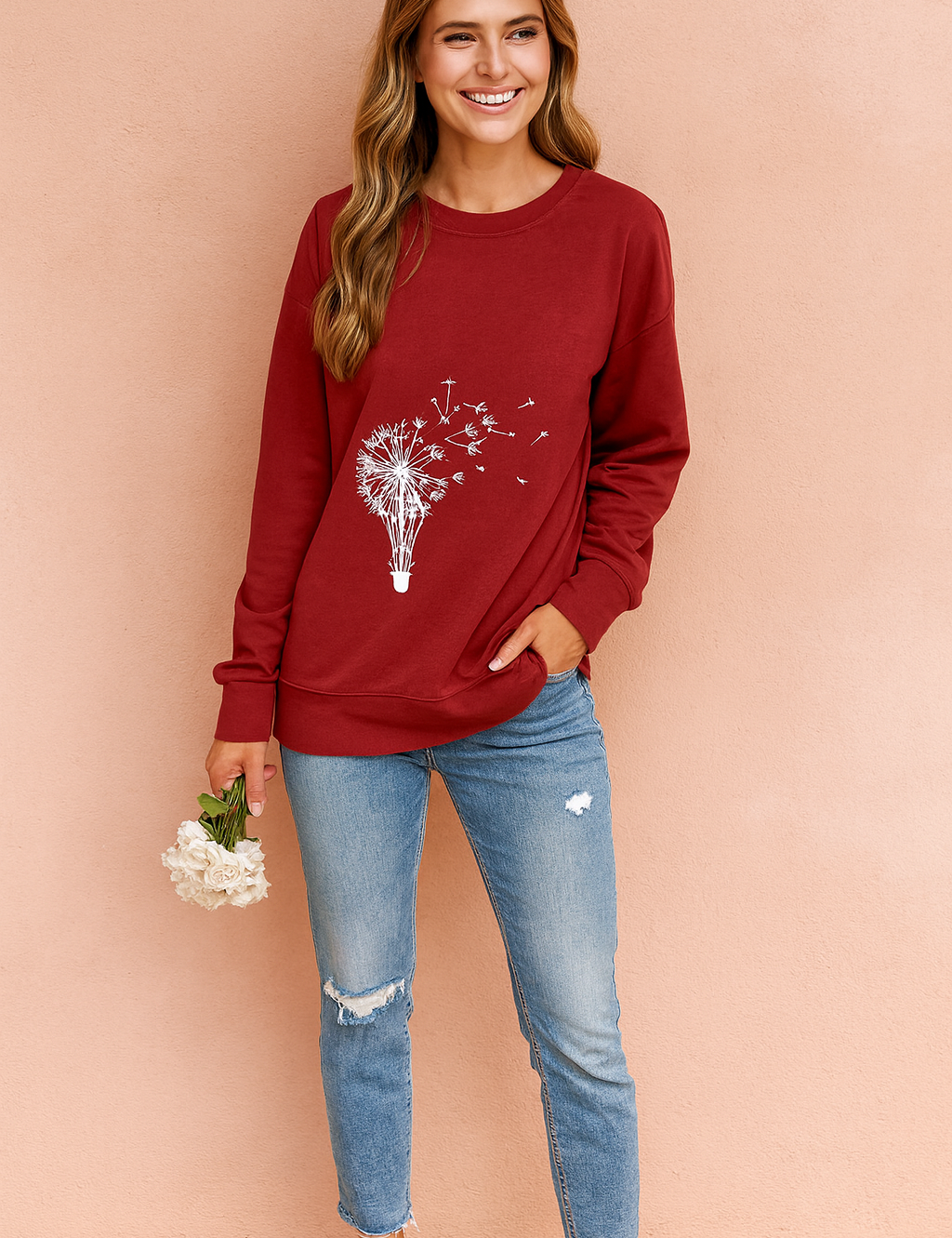Red long-sleeve sweatshirt with white dandelion and hot air balloon graphic, paired with fitted blue jeans and beige sneakers.