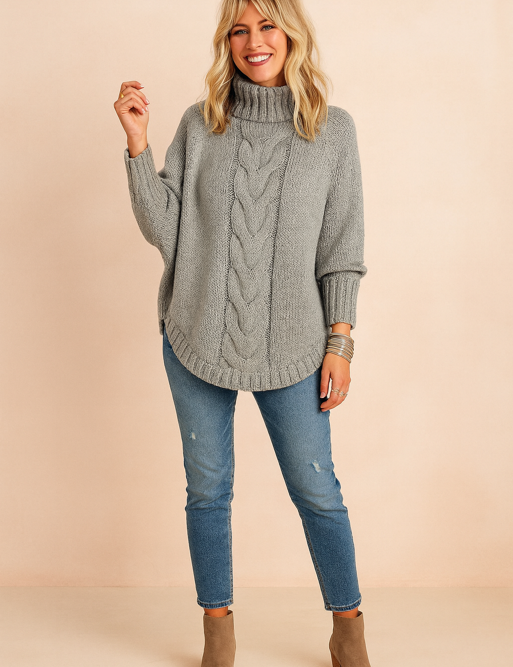 Oversized grey cable-knit turtleneck sweater with long sleeves, paired with medium-wash distressed skinny jeans and taupe suede ankle boots, accessorized with silver bangles.