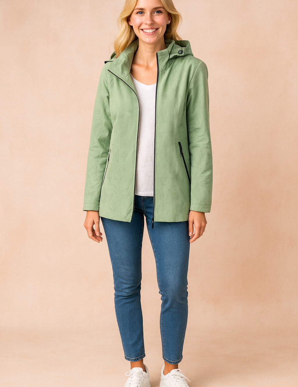 Women's sage green hooded parka jacket with subtle botanical print, front zipper closure, and zippered side pockets, styled with a white T-shirt, slim blue jeans, and white sneakers