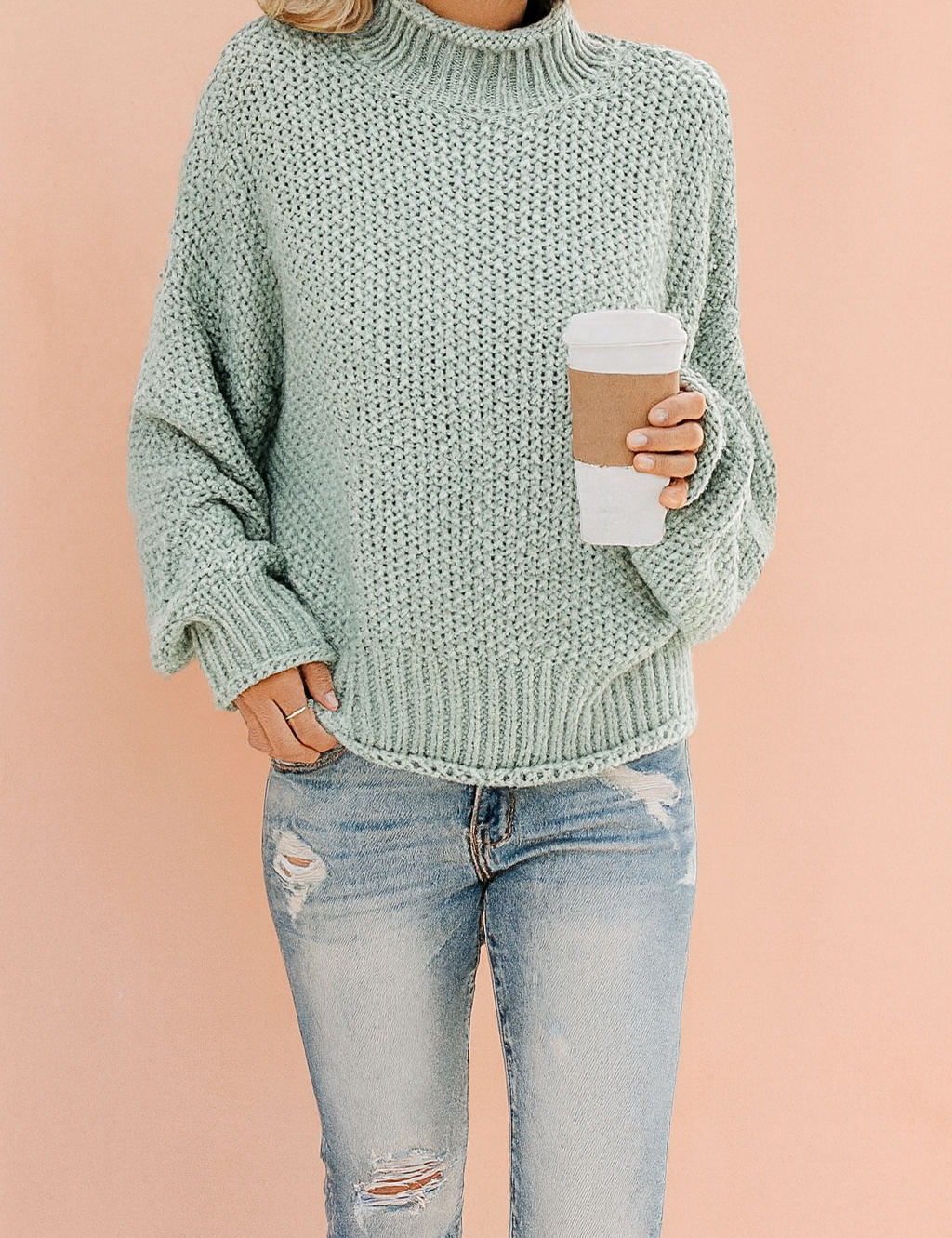 Light sage green chunky knit turtleneck sweater with ribbed cuffs and hem, paired with distressed light blue jeans.
