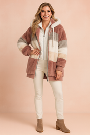 Striped faux fur hooded jacket in dusty rose, beige, white, and gray with ribbed cuffs and hem, styled over a white zip-up top and slim white pants paired with taupe suede ankle boots.
