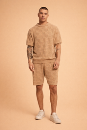 Men’s coordinated tan knit short-sleeve sweater and matching shorts set featuring a breathable geometric open-weave pattern, ribbed crew neckline, ribbed hem finish, relaxed tailored fit, and clean white low-profile sneakers for a refined summer casual look