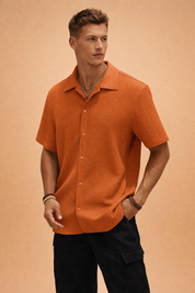 Short-sleeve textured button-up shirt with a relaxed open collar, straight hem, and matching front buttons, styled with black cargo trousers for a clean modern look.