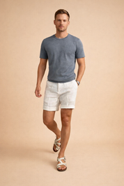 Lightweight white linen shorts with a clean tailored cut, smooth breathable fabric texture, straight hem above the knee, subtle natural linen weave, paired with a solid navy blue short-sleeve crew-neck cotton T-shirt with a matte finish and classic regular fit, styled with beige leather strap sandals featuring a flat sole and minimalist design.